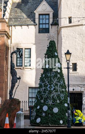 Dunbar, East Lothian, Scotland, United Kingdom, 7th November 2021. Christmas Lights erected: The High Street is closed to allow the Christmas lights to be put up across the main road through the town. Pictured: A Christmas tree outside the Town Hall next to the statue of John Muir as a boy Stock Photo