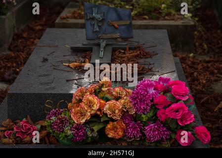 Autumn at cemetery. Faded leaves on grave and colorful artificial flowers. Eternal memory, mourning, grief concepts. Stock Photo