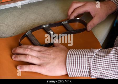 Shoemaker hands putting steel form on leather to make shoe insole on cutting machine in workshop. Leather crafting handmade shoes. Selective focus Stock Photo