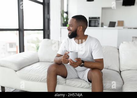 Smiling African American man drinking coffee sitting on couch Stock Photo