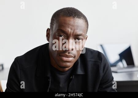 Close up portrait of serious African-American man in black looking at camera in minimal interior Stock Photo