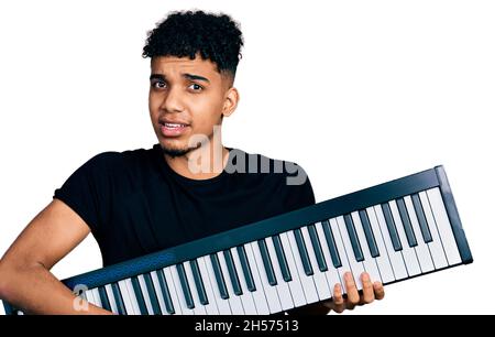 Young african american man holding piano keyboard clueless and confused expression. doubt concept. Stock Photo