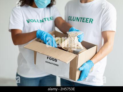 Female and male volunteers in protective gloves packing beans in cardboard box, working together on donation project Stock Photo