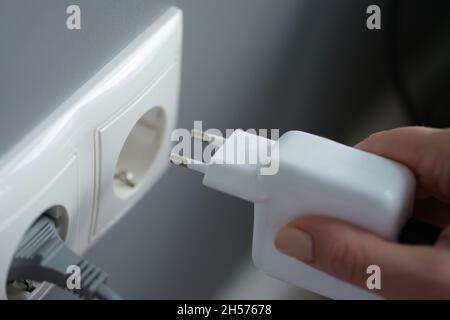Hands plugging the charger into an outlet in the wall, close-up Stock Photo