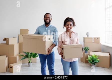 Satisfied happy young african american husband and wife carry boxes with belongings in new flat Stock Photo