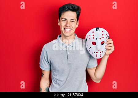 Young hispanic man wearing hockey mask looking positive and happy standing and smiling with a confident smile showing teeth Stock Photo