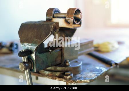 The metal product is squeezed in a vice at the workplace in the workshop. Workbench with old vises. Stock Photo