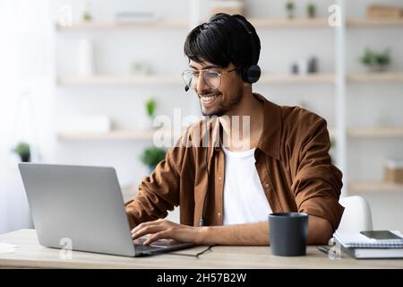 Happy indian guy attending webinar, typing on laptop keyboard Stock Photo