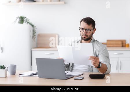 Concentrated busy mature caucasian man in glasses work with documents near laptop Stock Photo