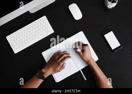 Minimal top view background of male hands writing in planner at black desk, copy space Stock Photo