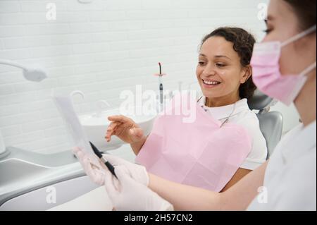Focus on a woman patient sitting in dentists chair, looking at the panoramic dental X-ray while dentist hygienist explains the consultation treatment Stock Photo