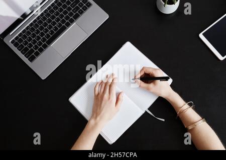 Minimal top view background of female hands writing in planner while working at black desk with laptop, copy space Stock Photo