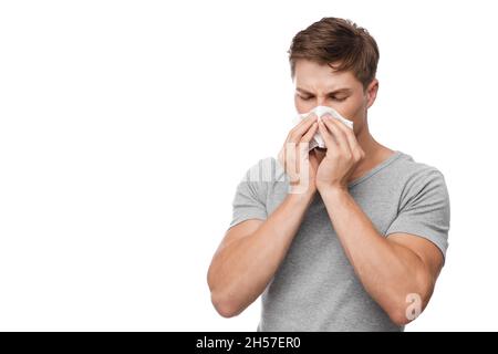Unhappy millennial european attractive man blows his nose in napkin and suffers from runny nose Stock Photo