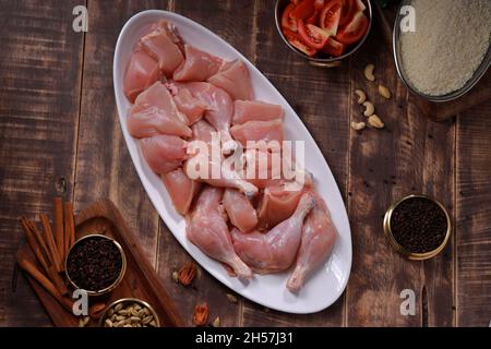 Raw chicken biriyani cut without skin arranged on white table ware with ingredients placed in the background with rustic wooden background. Stock Photo