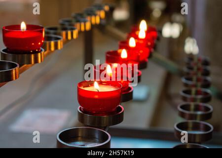 Burning red prayer candles inside a catholic church on a candle rack. Selective focus. Stock Photo