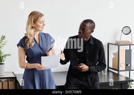Minimal waist up portrait of two business partners discussing project while standing by desk Stock Photo