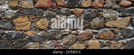 Old rough wall of multicolored natural stone. Abandoned building texture Stock Photo