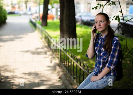 A teenage girl is talking on her cell phone while sitting in the square. Stock Photo