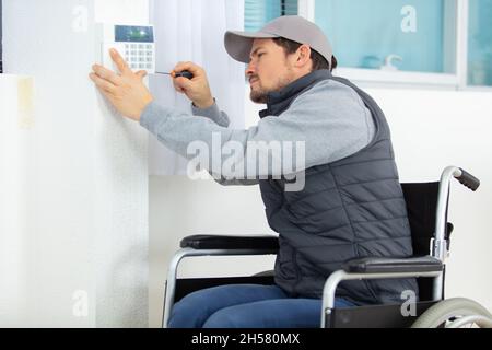 invalid young electrician installing security alarm on wall Stock Photo
