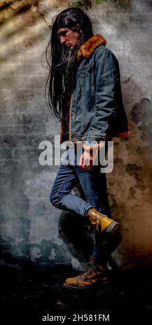 Black long hair man with jeans and big yellow shoes and old wall Stock Photo