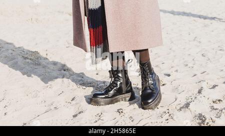 Stylish black smooth leather ankle boots in outdoor on the sand beach. Cold season outfit Stock Photo