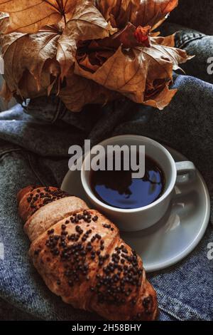 Aromatic black coffee americano in white cup and fresh sweet croissant with chocolate on denim background Stock Photo
