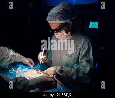 Female surgeon with an electrocoagulator over the patient's body during surgery. Selective focus. A doctor in 3D glasses, sterile gloves and a uniform operates with a surgical instrument. Stock Photo
