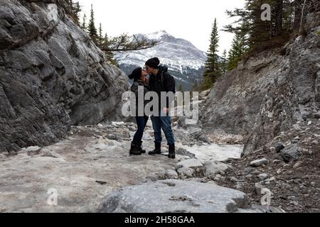 Couple standing on Grotto Mountain kissing. mountains in background. overcast sky. rocks, trees. Stock Photo