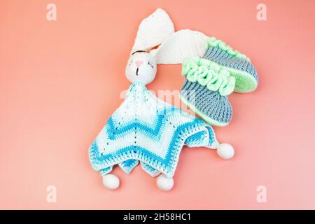 Handmade knitted blue and white bunny toy and grey and gtreen booties for premature babies isolated on pink background Stock Photo