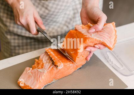 Butchering salmon, piece of salmon red fish meat. Woman in an apron prepares red fish fillets for cooking. Stock Photo