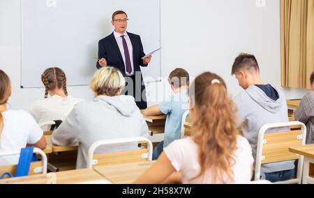 Man teacher with notebook is giving interesting lecture for students in classroom Stock Photo