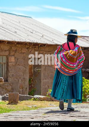 Indigenous Peruvian Quechua woman in traditional clothing walking in a street of Taquile Island by the Titicaca Lake, Peru. Stock Photo
