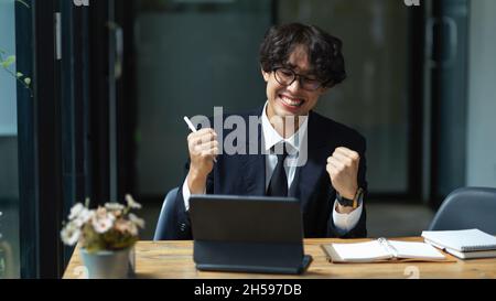 Asian young businessman extremely happy and satisfied on his project. Excited male executive at his desk. Work promotion. Stock Photo