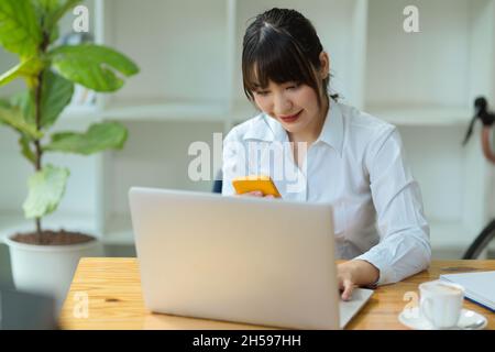 Female college student using smartphone for searching an informations while doing assignment on laptop. Stock Photo