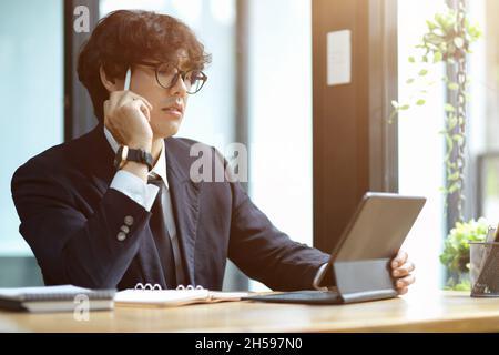 Focused young businessman working and pensive thinking on his project assignment while using tablet computer. Stock Photo