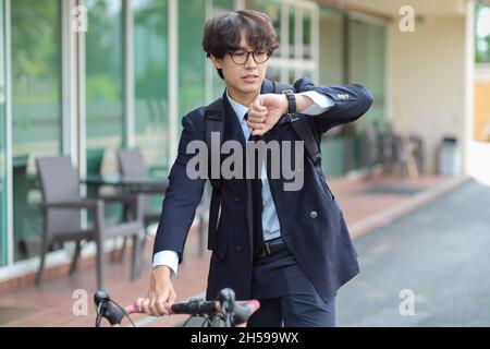 Urban millennial businessman looking at wristwatch while biking on a bicycle commuting to work. Stock Photo