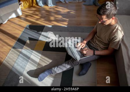 A young adult in eyeglasses is sitting on the floor and working  Stock Photo