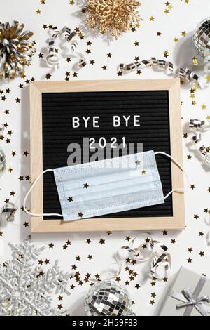 black letter board with text BYE BYE 2021 with decoration and mask on white background. Happy new ear 2022 concept. Stock Photo