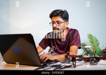 Man or student checking quadcopter or drone by connecting to laptop at laboratory - concept of UAV developing, Repairing or Experimenting. Stock Photo