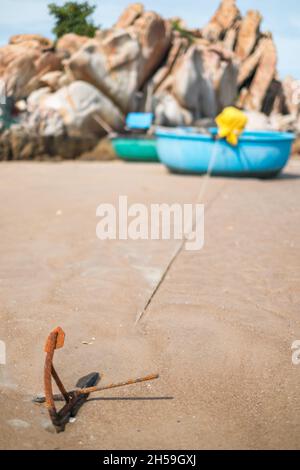 Round fishing boat stands with an anchor on the picturesque beach with large rocks. Rusty old anchor. High quality photo Stock Photo
