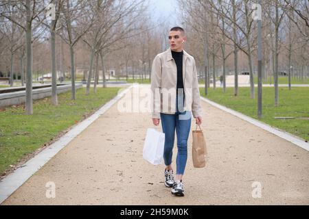 Young man wearing make up walking with shopping bags and listening music. Stock Photo