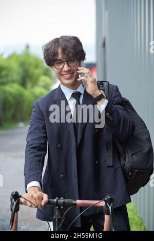 Portrait of asian businessman in business suit talking on the phone while going to work by bike. Stock Photo