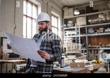Mature male carpenter looking at blueprints plans in carpentery workshop. Small business concept. Stock Photo