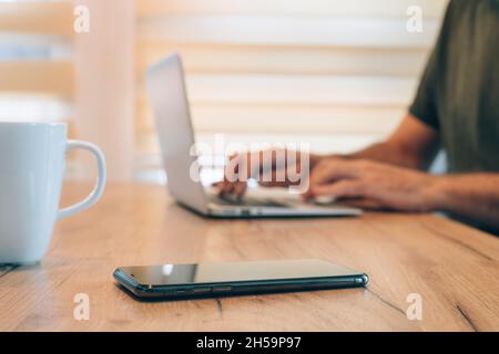 Work from home, smartphone on the desk, male hands typing laptop computer keyboard, selective focus Stock Photo