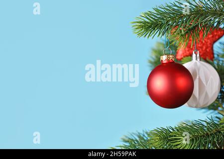 Ball shaped red Christmas baubles on Christmas tree on side of blue background with copy space Stock Photo