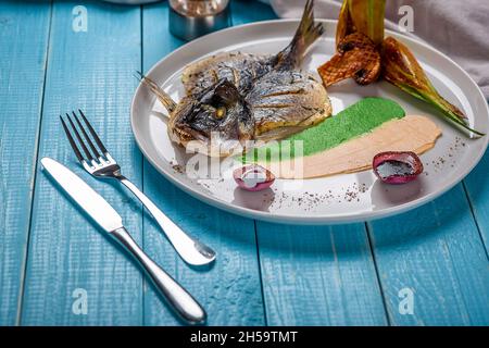 Fried fish dorado, decorated with cucumbers and onions. On a blue wooden background Stock Photo