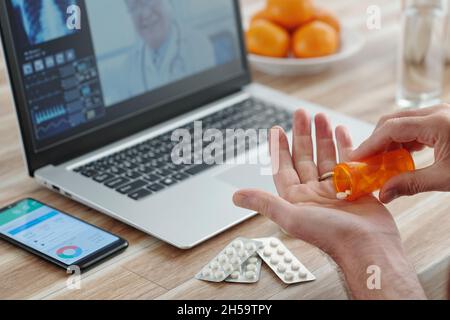 Hands of senior man using telemedicine website on laptop to talk to doctor and taking prescribed pills Stock Photo