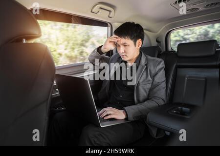 stressed young business man using laptop computer while sitting in the back seat of car Stock Photo