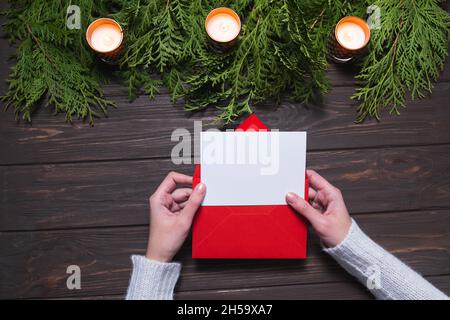 Woman's hands holding blank card and envelope on wooden background. Chritsmas design. Stock Photo