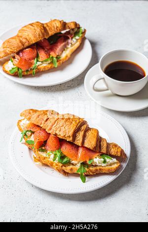 Croissant sandwich with cream cheese, salmon and arugula on a white plate, gray background. Healthy breakfast concept. Stock Photo